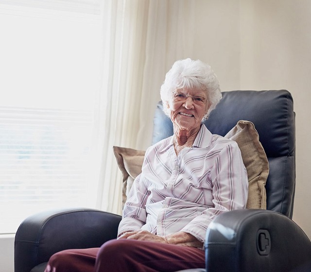 ddynes oedrannus yn eistedd ar cadair edrych try'r ffenest.